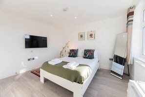 A bedroom with a bed, a flat-screen TV, a mirror, and a window with curtains.