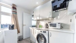 A compact kitchen with a washing machine, microwave, and a coffee maker. - Modern Surrey Studio - Easy Access to London (Surrey)