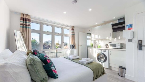 A hotel room with a bed, a washing machine, a microwave, and a view of the outdoors. - Modern Surrey Studio - Easy Access to London (Surrey)