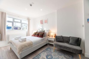 A bedroom with a bed, bedside table, lamp, and a grey sofa.
