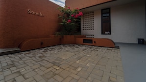 Ein Innenhof mit Pflastersteinen, einer Mauer mit der Aufschrift 'Soocha' und einem Blumentopf mit rosa Blüten.