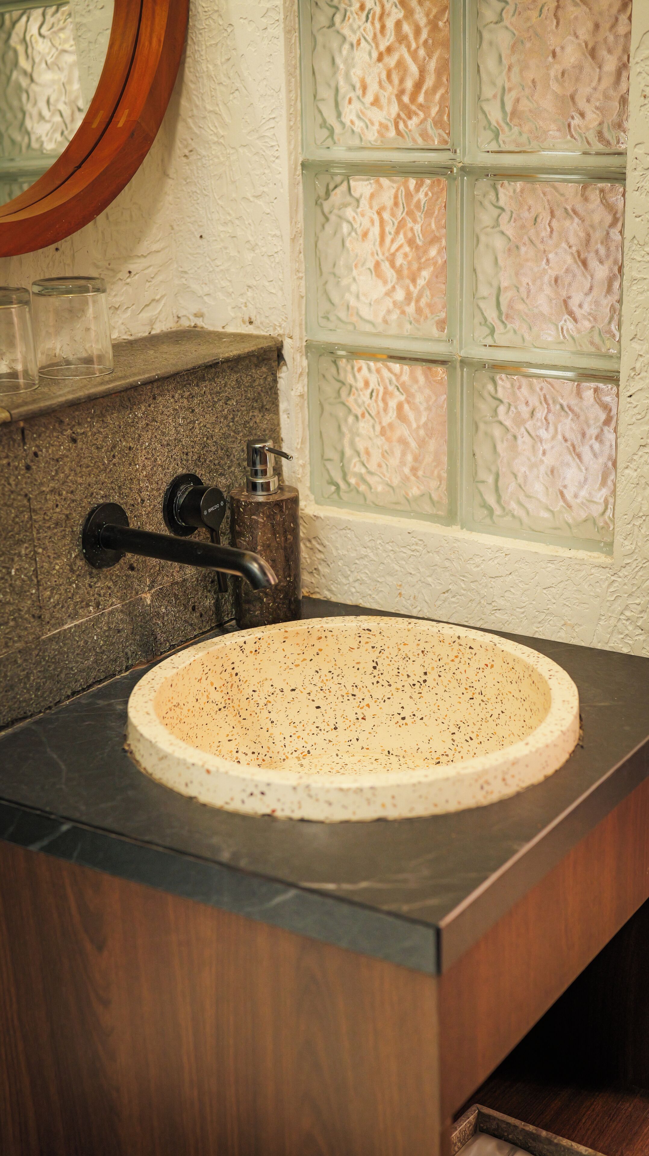 A bathroom with a round sink, a mirror, and a window with textured glass.