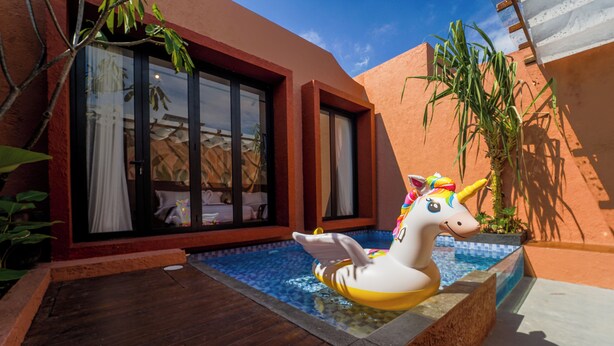 Ein Swimmingpool mit einem Einhorn-Schwimmtiermodell, einer Holzterrasse und einem Gebäude mit großen Fenstern und roter Außenfassade.