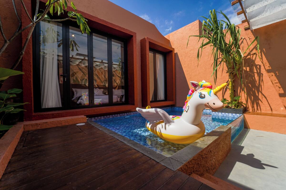 A swimming pool with a unicorn float, a wooden deck, and a building with large windows and a red exterior.