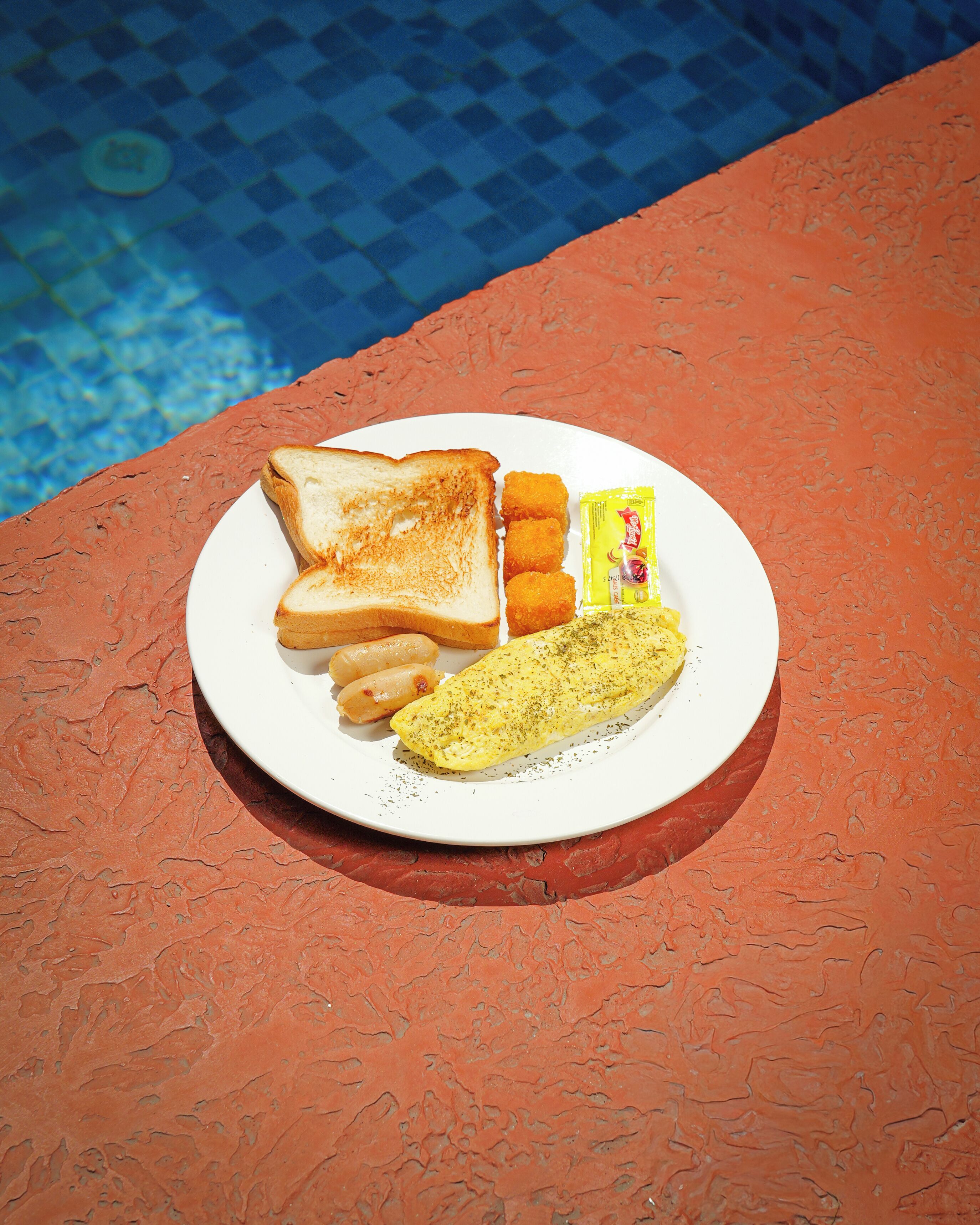 Une assiette contenant des tranches de pain grillé, des saucisses et un œuf au plat, le tout posé sur une surface orange texturée.