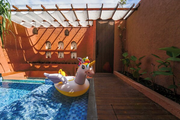 Una piscina con un flotador de unicornio, una cubierta de madera y un edificio con ventanas arqueadas.