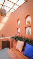 Una habitación con un banco de madera, un lavamanos y una ventana con celosía de metal.