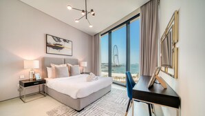 A modern hotel room with a large bed, bedside lamps, a desk, and a view of a distant landmark. - Classy Address JBR 3BR w/ Balcony and Beach Access (Dubai)