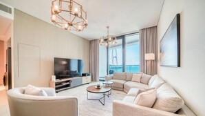 A modern living room with a sofa, armchairs, a coffee table, a TV, and a large window with a view of a Ferris wheel. - Classy Address JBR 3BR w/ Balcony and Beach Access (Dubai)