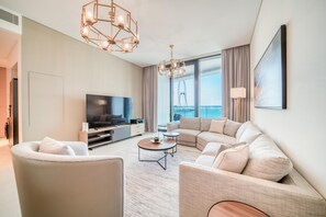 A modern living room with a sofa, armchairs, a coffee table, a TV, and a large window with a view of a Ferris wheel. - Classy Address JBR 3BR w/ Balcony and Beach Access (Dubai)