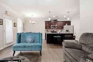 A modern kitchen with dark cabinets, a microwave, and a refrigerator. There is a blue armchair with a decorative pillow and a gray sofa. - Modern Dallas Retreat ~ Spacious 3BR + 2.5BA (Dallas)
