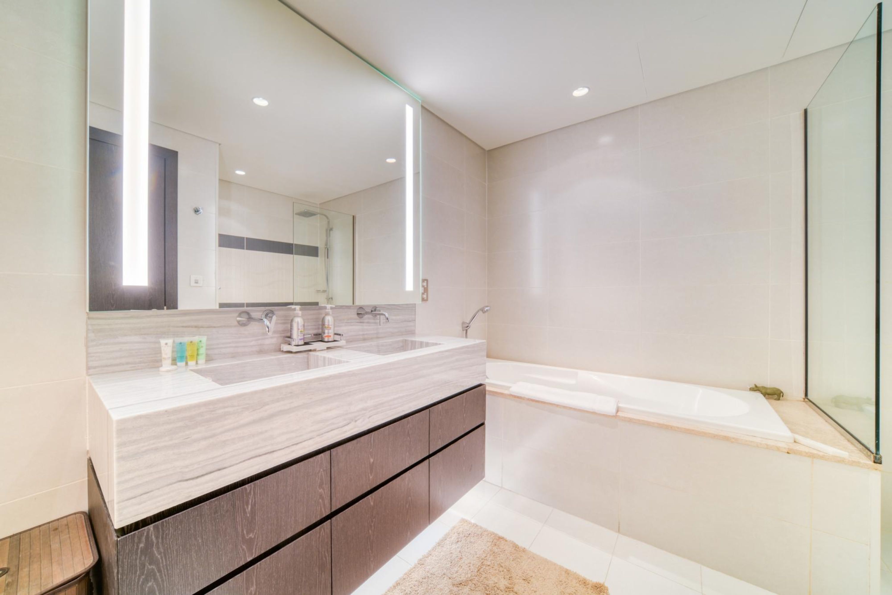 Ein modernes Badezimmer mit großem Spiegel, zwei Waschbecken, einer Badewanne und einer Holzausstattung.