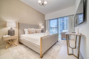 A modern hotel room with a large bed, a bedside table with a lamp, a small desk, and a large window offering a city view. - Modern Elegance w/ a New York Edge DIFC Apt (Dubai)