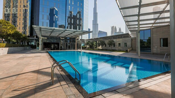 A swimming pool with a metal railing, surrounded by modern buildings and a clear sky. - Modern Elegance w/ a New York Edge DIFC Apt (Dubai)