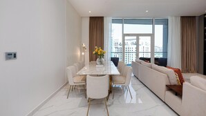 En moderne stue med et marmorgulv, et spisebord med stole, en sofa og et stort vindue med gardiner.