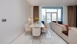 Una sala de estar moderna con suelo de mármol, una mesa de comedor con sillas, un sofá y un amplio ventanal con cortinas.
