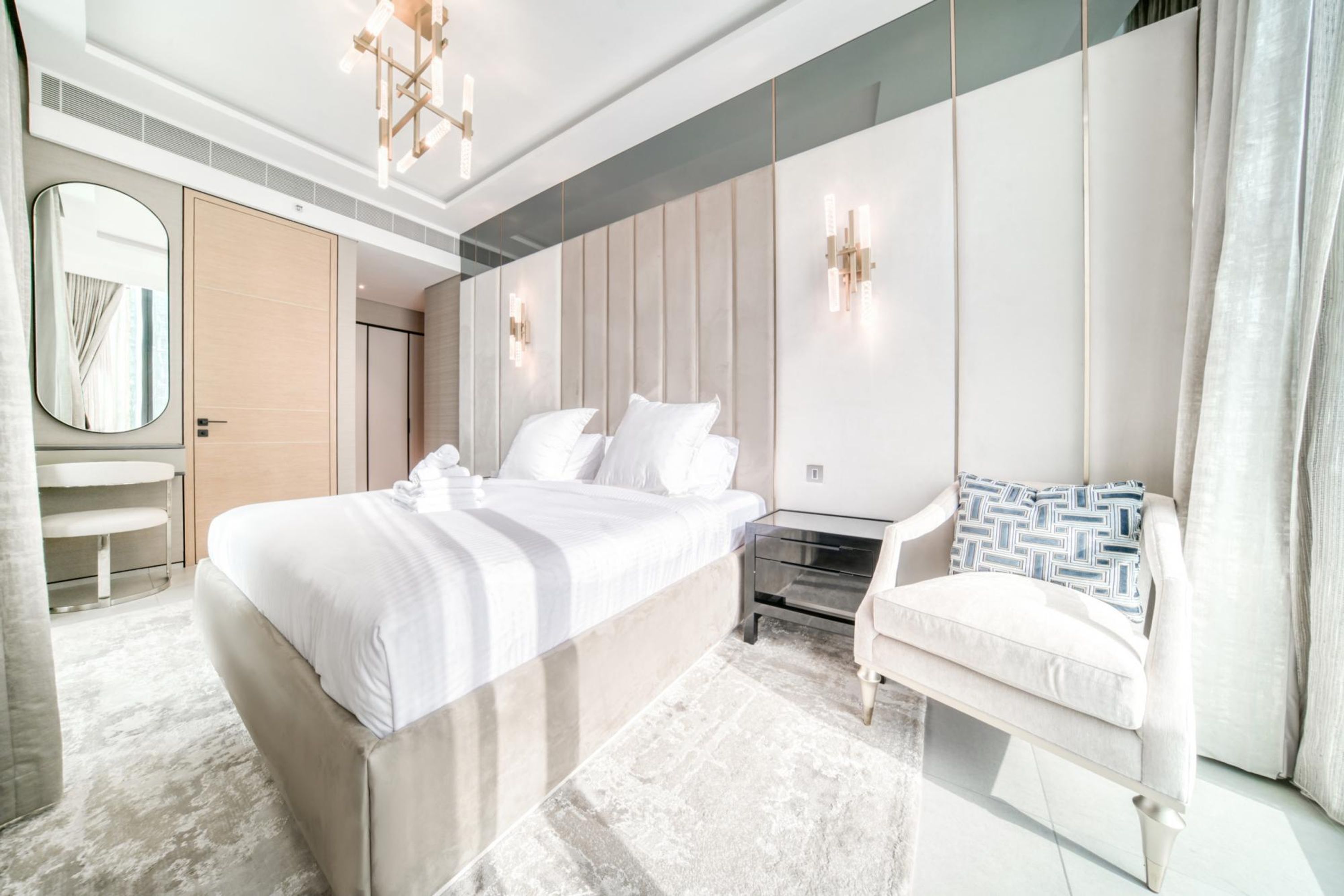 Una habitación de hotel moderna con una cama grande, una zona de estar, un espejo y un armario.