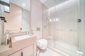 Un bany modern amb plat de dutxa de vidre, un lavabo blanc i un vàter.