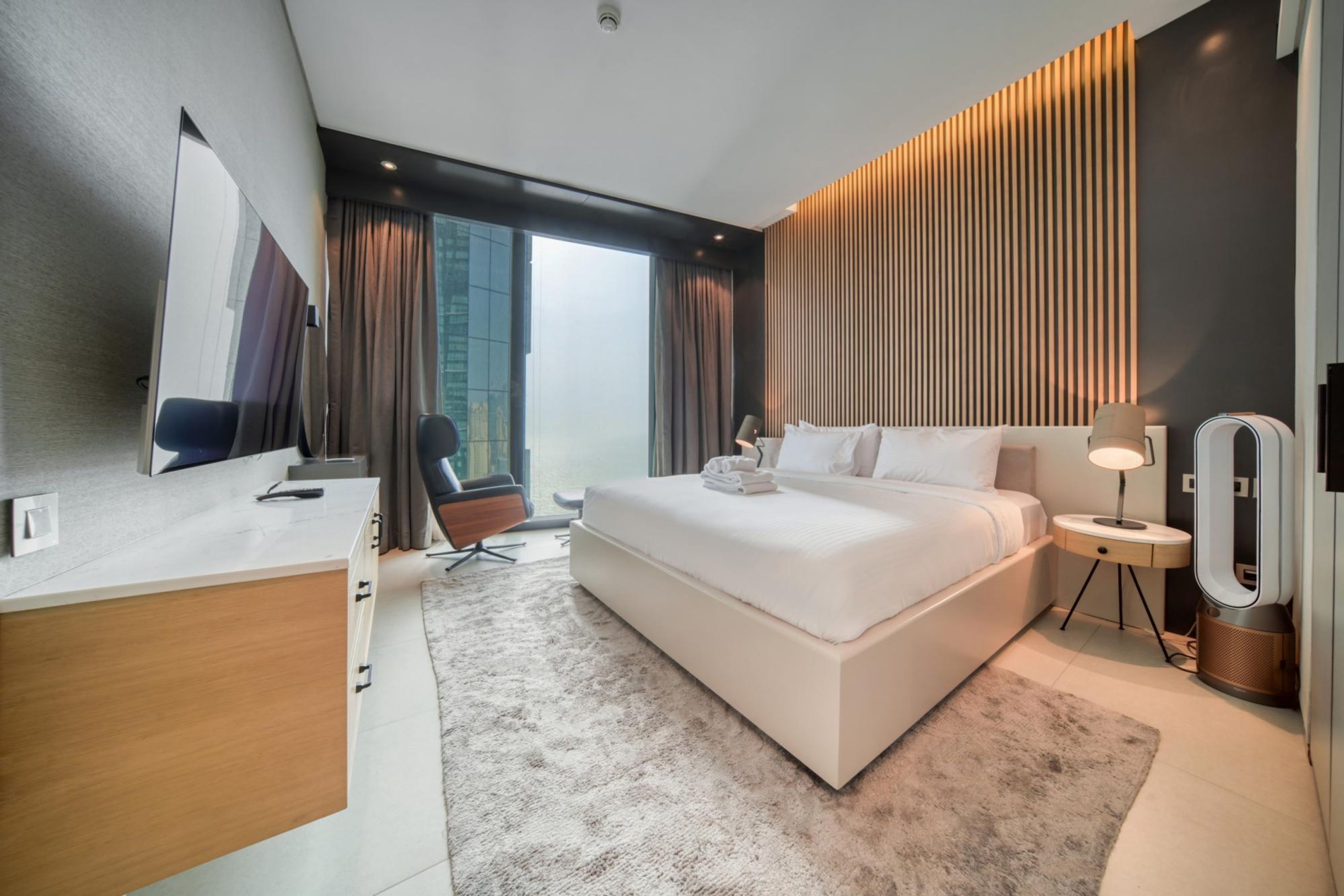 Een moderne hotelkamer met een groot bed, een bureau, een stoel, een nachtkastje met een lamp en een spiegel.