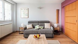 Een moderne woonkamer met een grijze bank, een houten salontafel met fruit, een radiator, een ingelijste botanische print en een roze wand.