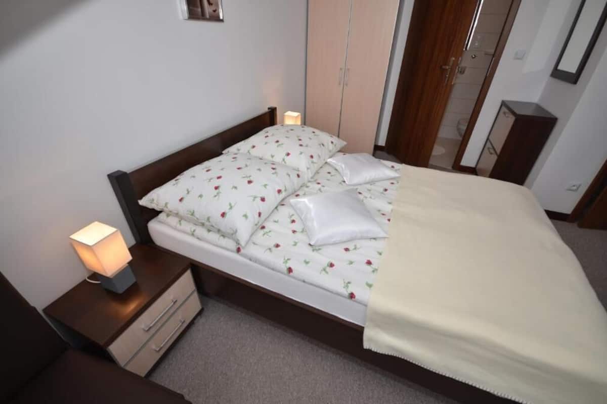 Ein ordentlich bezogenes Bett mit floralem Bettzeug, einer Nachttischlampe und einem Holz-Kopfteil.