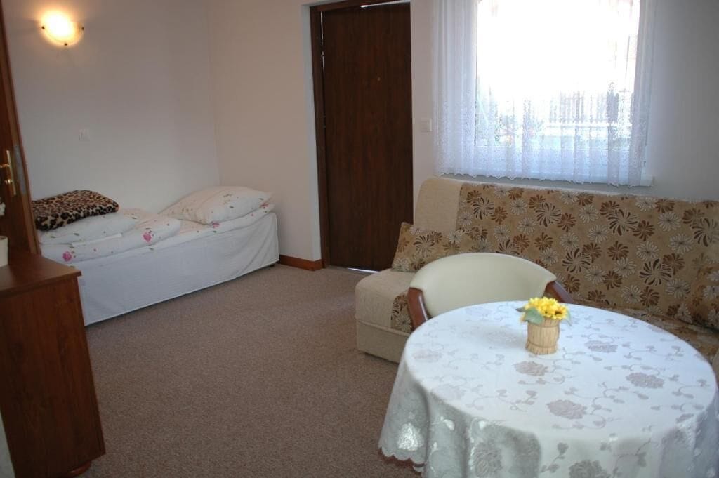 Un dormitorio con cama, sofá, una mesa con un florero y una ventana con cortinas.
