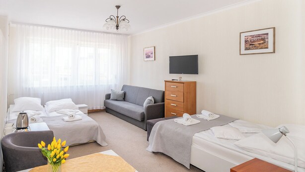 A hotel room with two beds, a sofa, a TV, a wooden dresser, and a vase with flowers. - Dom Wczasowy Isabelle (Darłowo)