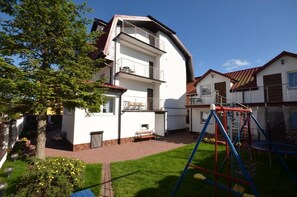A two-story residential building with a balcony, a fenced backyard, and a swing set. - Dom Wczasowy Isabelle (Darłowo)