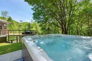 Ein Whirlpool, umgeben von üppigem Grün, einer Holzdielen-Terrasse und einem Gebäude mit Blick auf die Bäume.