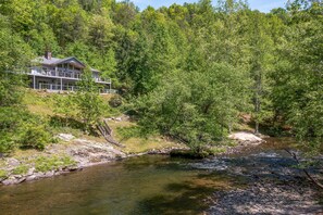 A house with a balcony overlooking a river, surrounded by dense forest. - River Vibes (Sevierville)