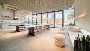 Ein modernes Interieur mit einem langen Gemeinschaftstisch, einer Sitzgruppe und großen Fenstern mit Blick auf die Stadt.