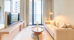 Un salon moderne avec un canapé, une table basse, un téléviseur posé sur un meuble et de grandes fenêtres avec des rideaux.