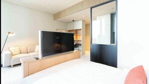 Quarto de hotel moderno com uma cama grande, televisão de tela plana, sofá e escrivaninha.