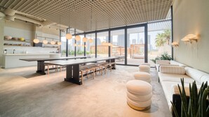 Um interior moderno com uma longa mesa comunitária, área de estar e amplas janelas com vista para a cidade.