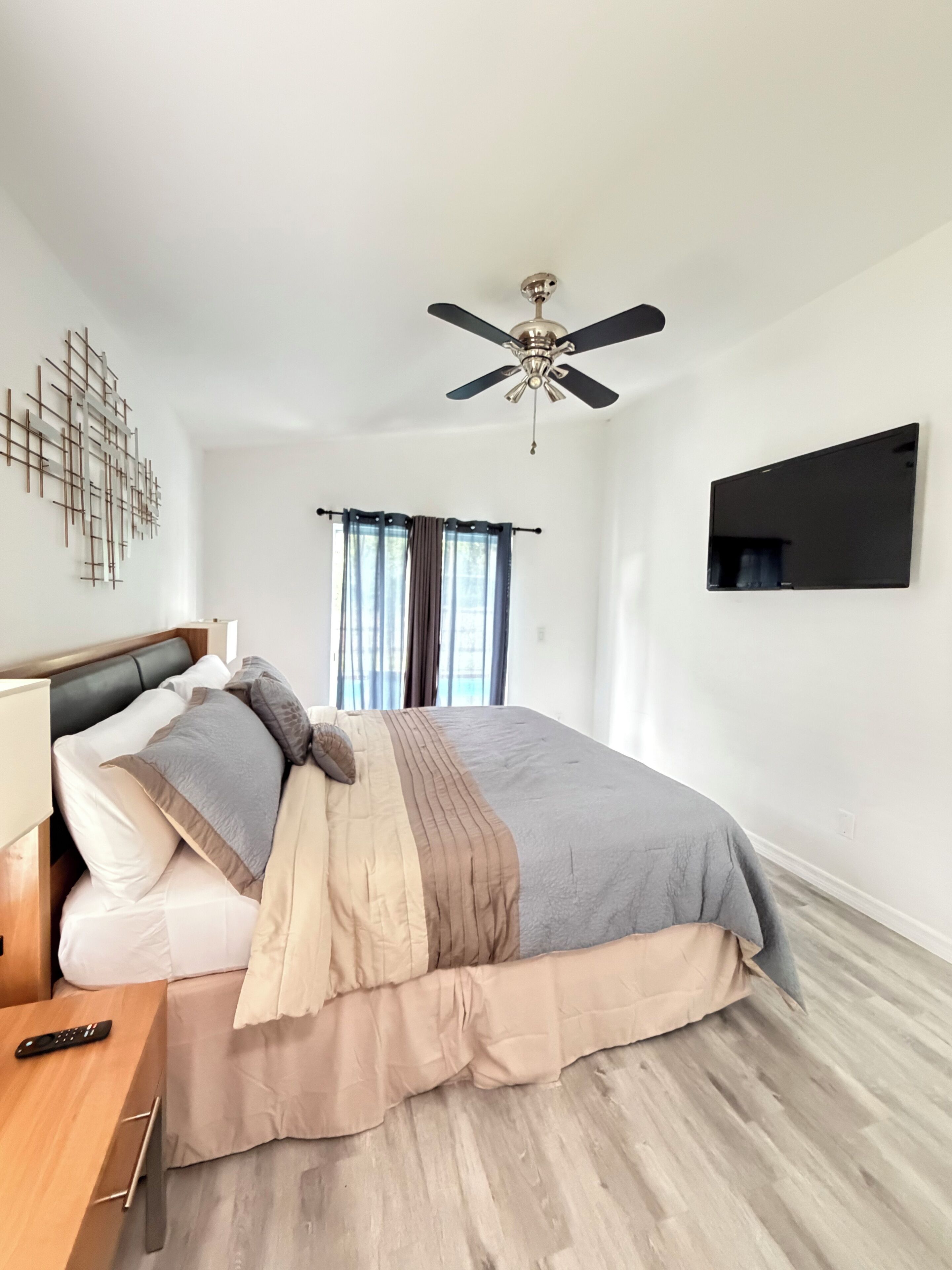 A bedroom with a bed, a ceiling fan, a mounted TV, and a window with curtains.