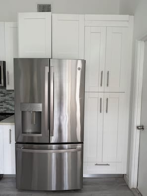 Ein Edelstahl-Kühlschrank mit Wasserspender, weißen Schränken und einer gefliesten Spritzschutzwand.