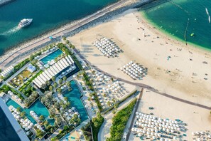 Vista aérea de um resort com uma grande piscina, área de praia e vários guarda-sóis.