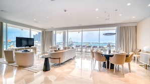 A modern hotel room with a large window, a flat-screen TV, a sofa, a dining table, and chairs. - FIVE Palm Jumeirah: 4BR Penthouse w/ Private Pool (Dubai)