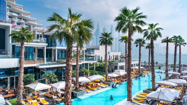 A rooftop pool area with palm trees, sun loungers, and a view of the city skyline. - FIVE Palm Jumeirah: 4BR Penthouse w/ Private Pool (Dubai)