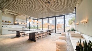 Ein modernes Interieur mit einem langen Esstisch, Sitzgelegenheiten und Blick durch große Fenster.