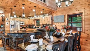 A spacious kitchen with wooden cabinets, a large island, and a dining area with chairs and a table set for a meal. - Heaven's Edge (Gatlinburg)