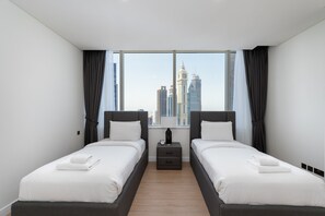 Habitación de hotel con dos camas, una mesita de noche y un ventanal con vistas a la ciudad.
