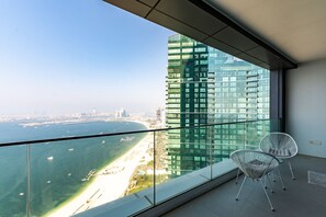 A balcony with a glass railing, two white wire chairs, and a view of a tall building and a beach. - Address JBR Elegant 2BR w/ Beach Access (Dubai)