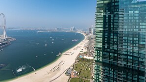 A coastal cityscape with a modern high-rise hotel, a beach, and a large Ferris wheel in the background. - Address JBR Elegant 2BR w/ Beach Access (Dubai)