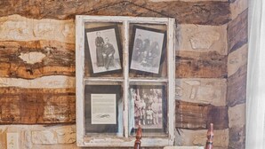 Interior rústico de una cabaña de troncos con una mecedora, un ventanal de madera con fotografías enmarcadas y una alfombra roja.