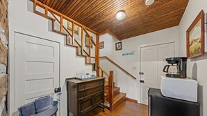 Una cocina con suelo de madera, una escalera con barandillas de madera, una cafetera y un refrigerador.