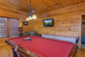 A pool table with a red felt surface, wooden walls, and a television mounted on the wall. - Eternally Yours (Gatlinburg)