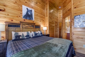 A wooden cabin interior with a bed, wooden walls, a headboard with a bear design, and a bear picture on the wall. - Eternally Yours (Gatlinburg)
