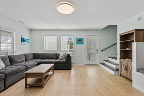 Ein Wohnzimmer mit Ecksofa, Couchtisch aus Holz, einer Treppe und einem Holzkabinett.