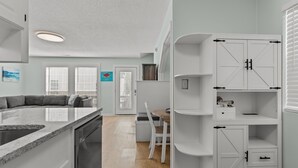 Eine moderne Küche mit integriertem Geschirrspüler, einem Essbereich mit weißem Tisch und Stühlen sowie einem weißen Schrank mit Schubladen und Regalen.